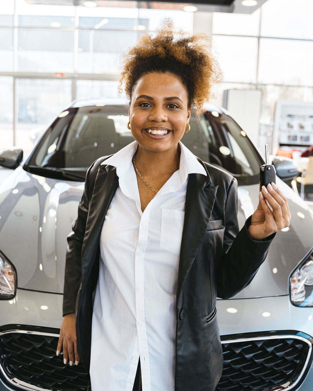 A smiling client holds up the key to her new silver SUV in a bright showroom